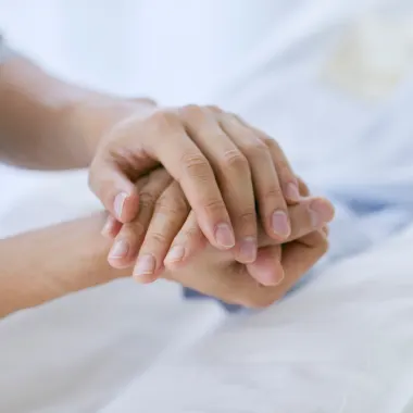 Two hands gently holding another hand, conveying comfort and support. The scene suggests a caring, empathetic interaction in a calm environment.