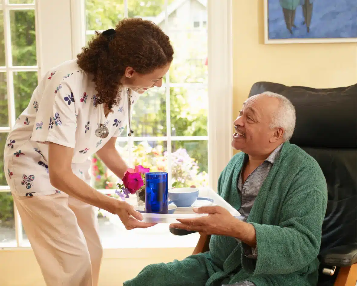 Caregiver serving meal to elderly man at home